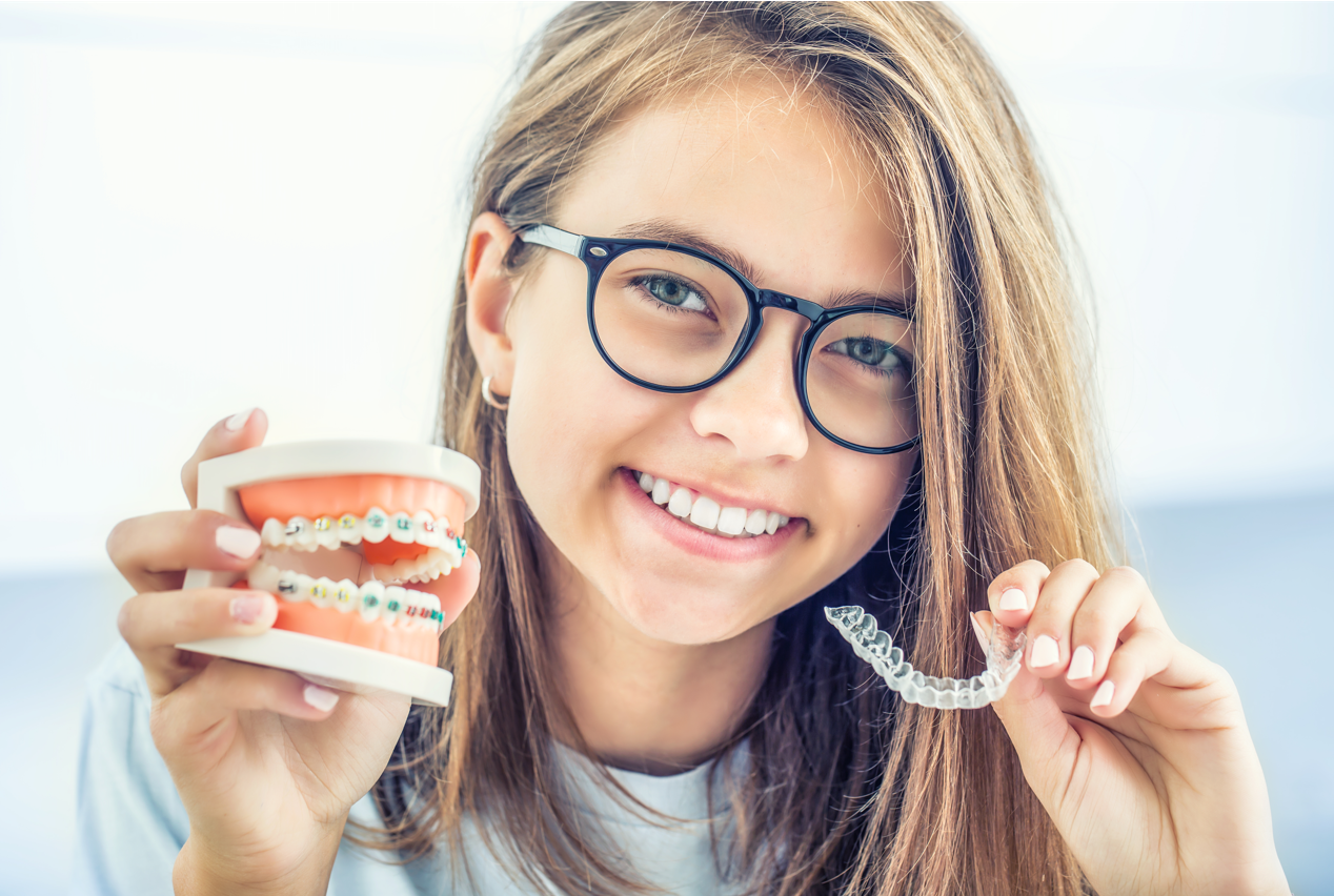 girl holding clear aligner and braces in each hand